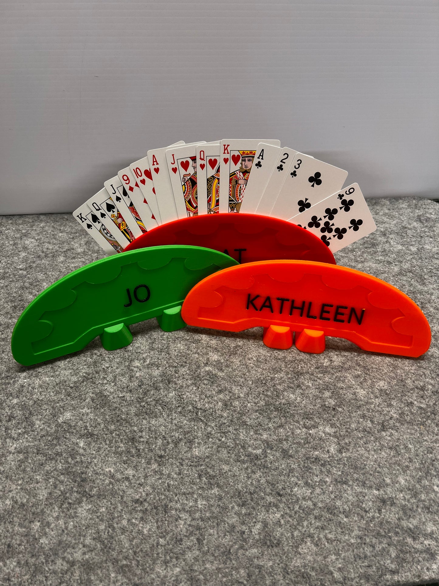 Playing cards fanned out next to a red and green card holder on a gray surface
